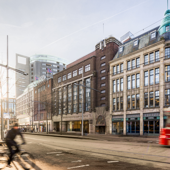Facade of University Campus Spui with cyclists and tram in the foreground.