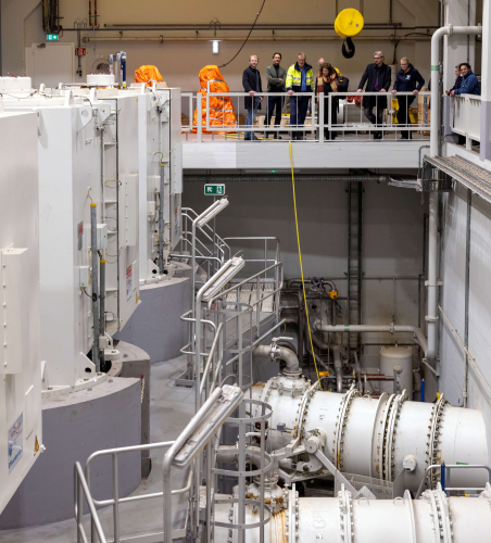 A modern technical space with equipment and visitors on the upper floor.