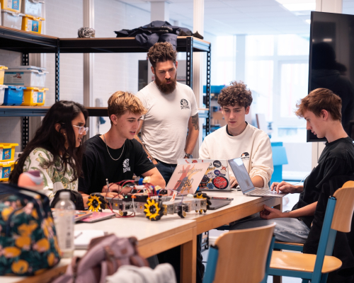 A group of high school students working on a robot with their coach.
