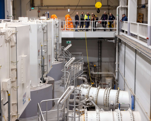 A modern technical space with equipment and visitors on the upper floor.