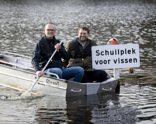 Two men sit in a boat next to a sign reading 'Shelter for fish'. Credit: Henriette Guest 