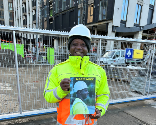 A man in bright work clothes holding a poster.