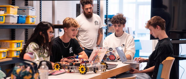 A group of high school students working on a robot with their coach.