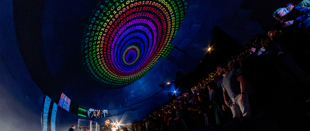 A band performs on stage with colorful light effects and a large visual projection.