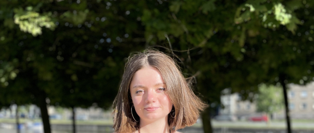 Profile picture of Olga, she has brown hair and there are trees in the background. 