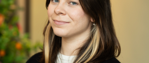 A woman with long brown hair and a black-and-white sweater smiles gently.