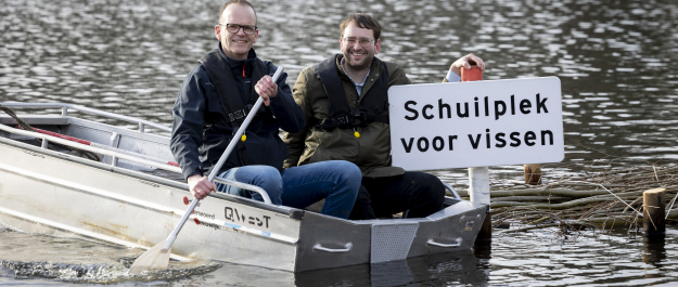 Two men sit in a boat next to a sign reading 'Shelter for fish'. Credit: Henriette Guest 