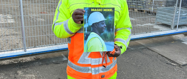 A man in bright work clothes holding a poster.