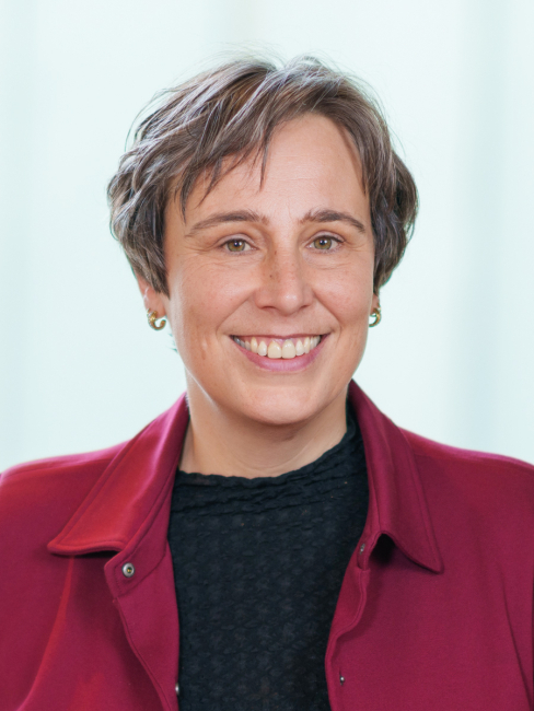 Woman smiling with short brown hair and a red jacket.