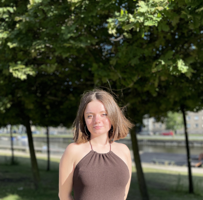 Profile picture of Olga, she has brown hair and there are trees in the background. 