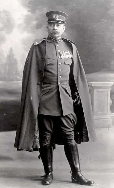 Full-length portrait of Major Lodewijk Thomson in formal military uniform with high boots, decorated medals, and a long cape. He stands in a studio setting with a painted backdrop, exuding authority and poise.