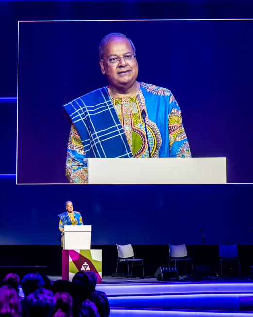 A man in traditional African attire speaks from a podium.