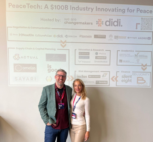 Two people stand in front of a presentation about PeaceTech.