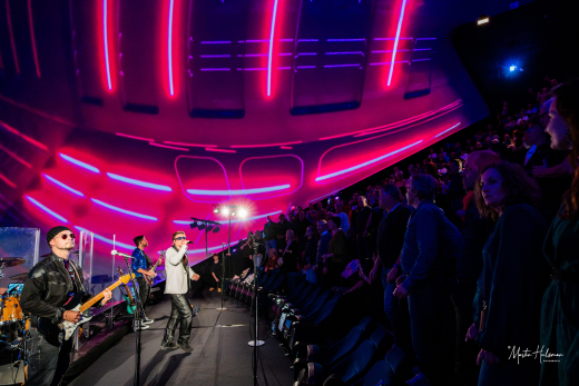 A band performs on stage with colorful lights and an enthusiastic audience.