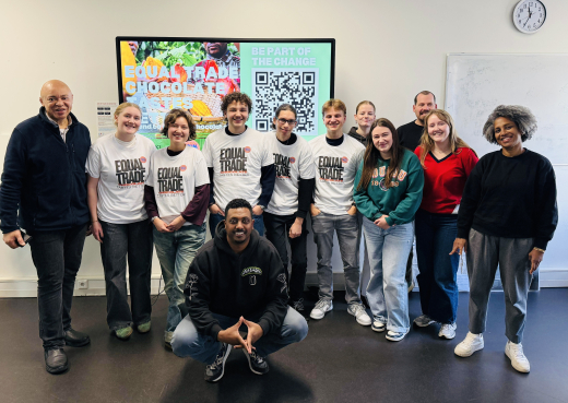 A diverse group of people wearing Equal Trade t-shirts stands in front of a screen with information.